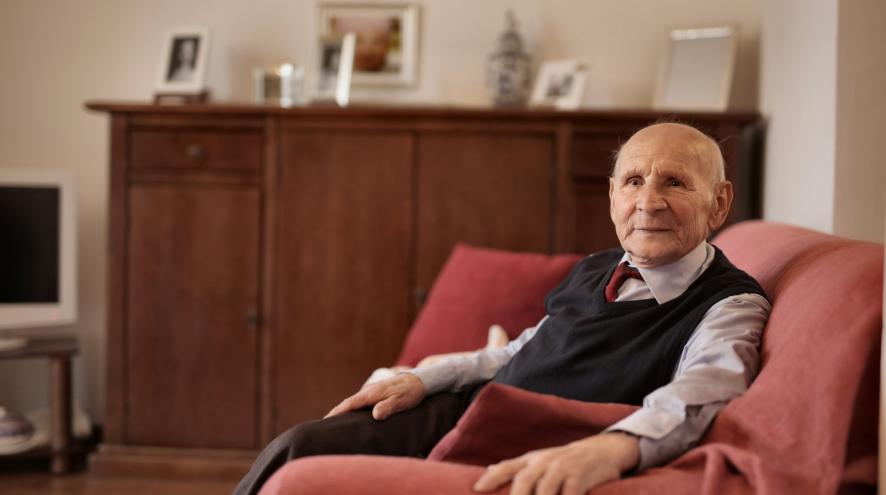 Elderly man sitting in a sofa, looking up at the camera.