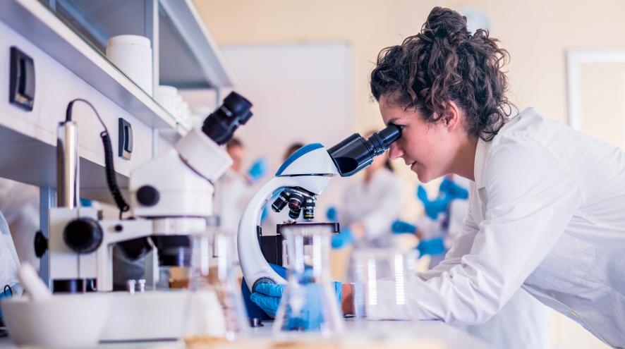 Female scientist looking at microscope in lab.