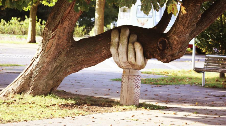 Carved wooden hand holding up tree branch