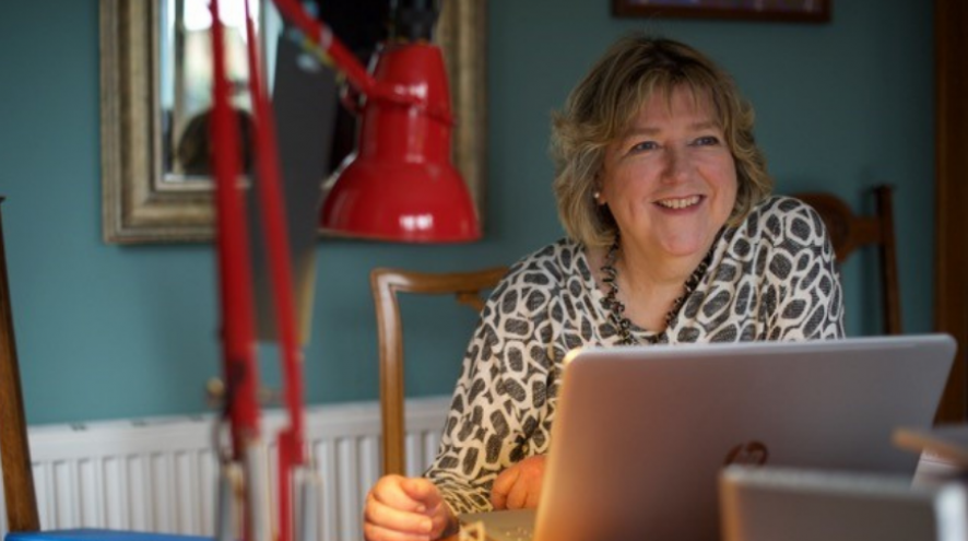 Prof. June Andrews sitting at her desk with a red reading lamp, a gold mirror and a laptop